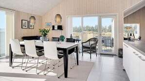 Une cuisine moderne dotée d’un grand îlot central, d’un coin repas avec une table et des chaises, et offrant une vue sur l’extérieur grâce à de grandes portes coulissantes.