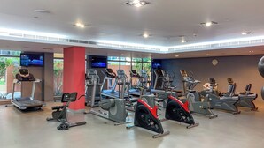 Un gimnasio con diferentes máquinas de cardio, una pantalla de televisión y un ventanal grande.
