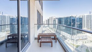 Un balcón con banca de madera y barandilla de vidrio que da a una vista panorámica de la ciudad con edificios modernos.