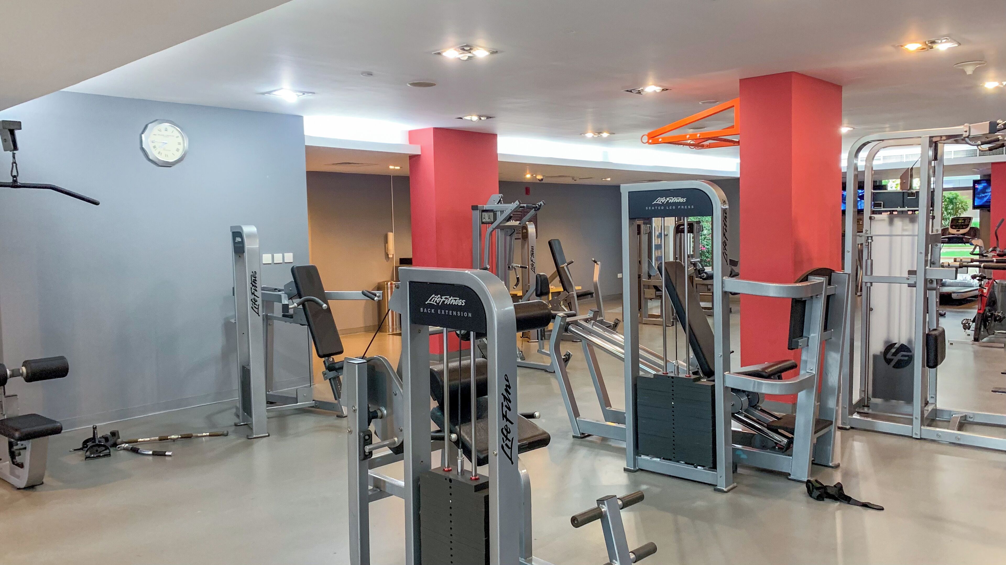 A gym with various exercise machines, a clock on the wall, and a red pillar.