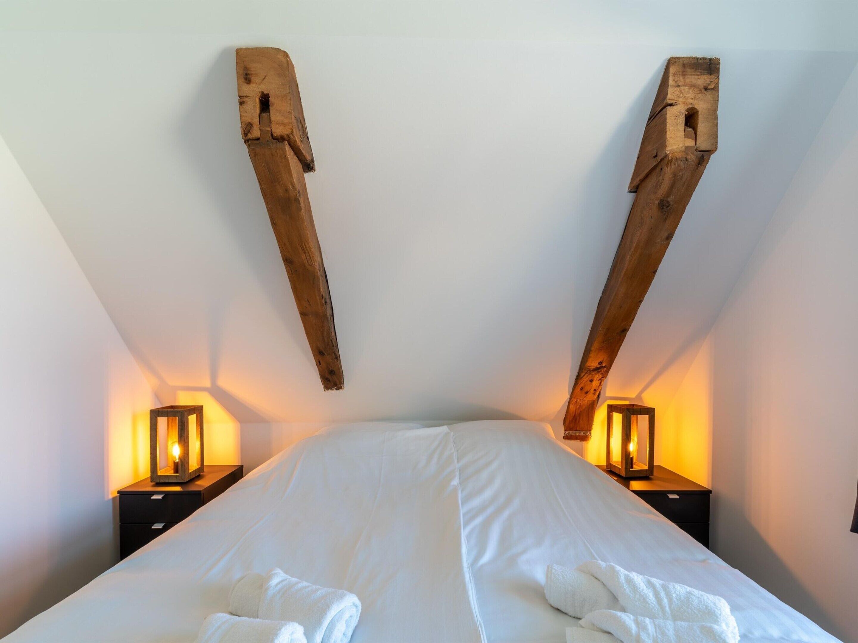 A bedroom with a large bed, wooden beams on the ceiling, and two bedside lamps.