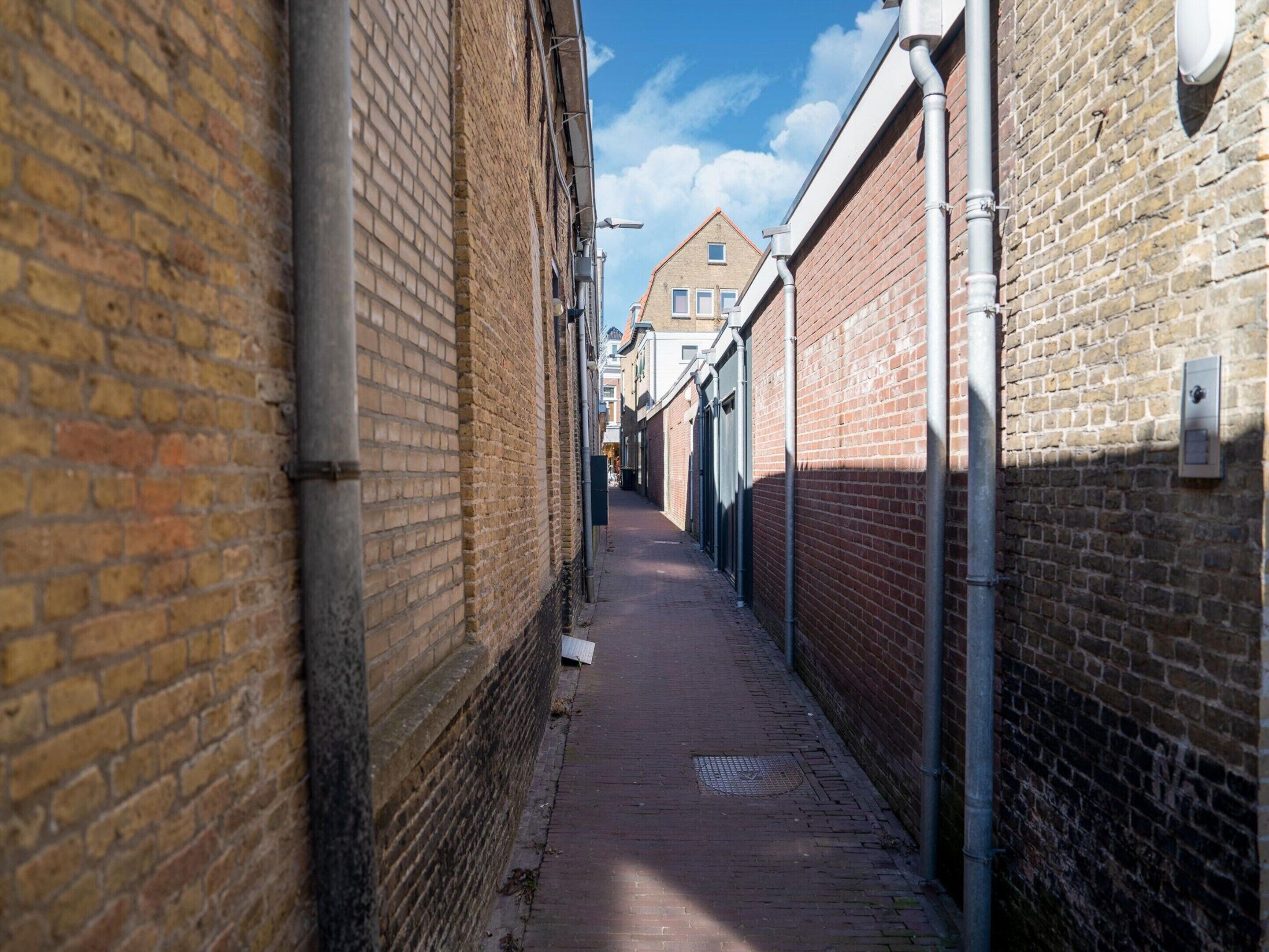 Une ruelle étroite aux murs de briques et au chemin pavé.