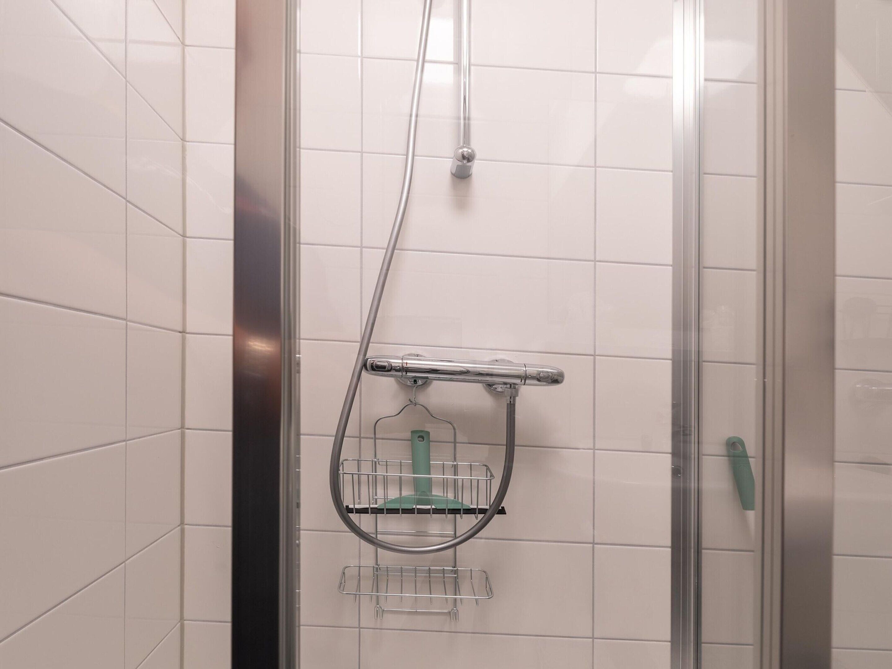 Eine Dusche mit Glastür, ein chromfarbener Duschkopf und ein grüner Handbrause.