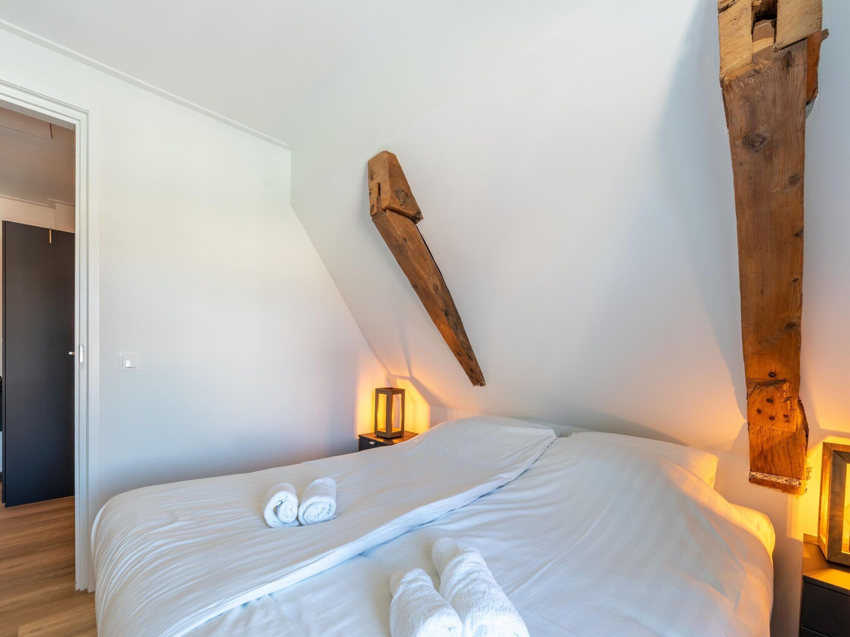 Un dormitorio con una cama grande, vigas de madera y una mesita de noche con lámpara.