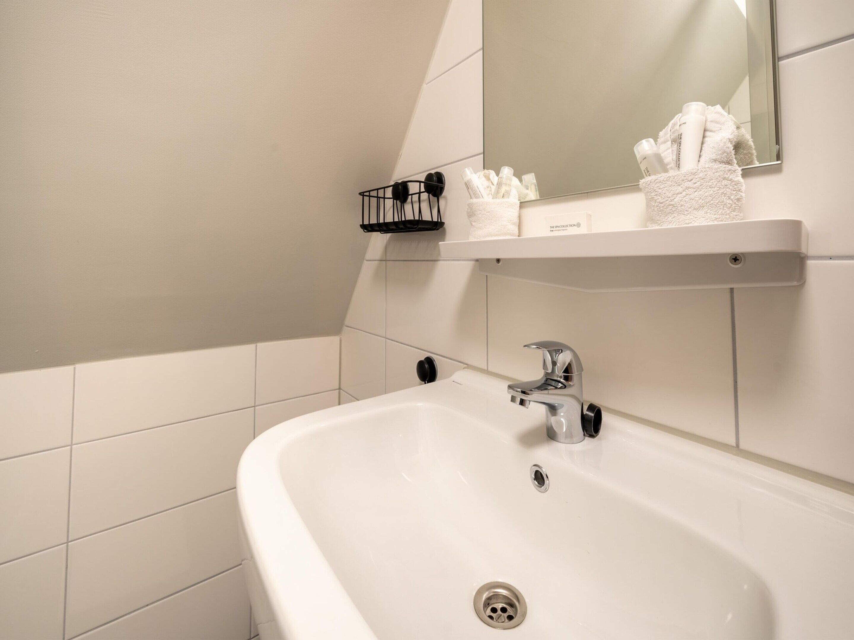 A bathroom with a white sink, a mirror, and a towel rack with toiletries.