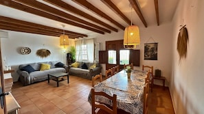 Ein geräumiges Wohnzimmer mit einem langen Esstisch, zwei Sofas und Holzbalken an der Decke.