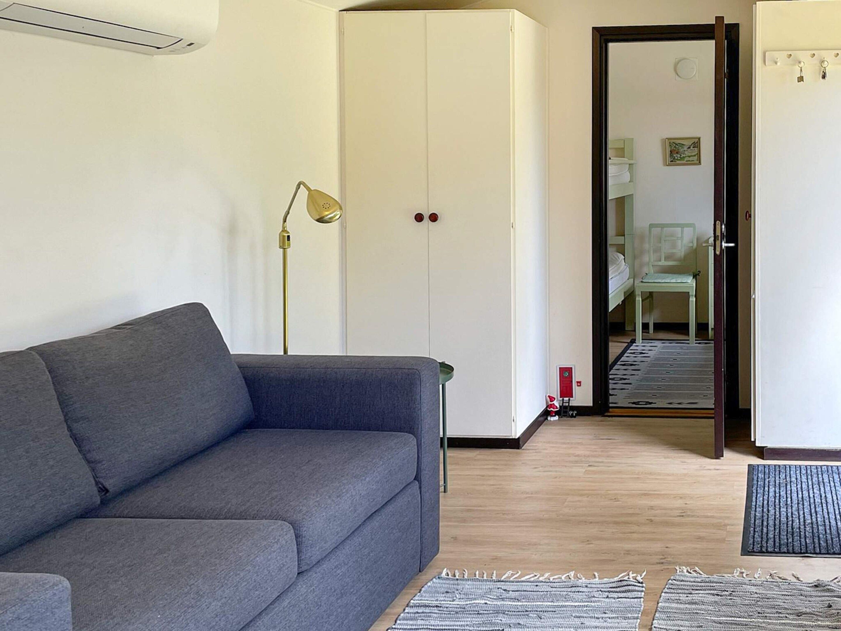A room with a grey sofa, a white wardrobe, a floor lamp, and a door leading to another room.