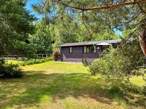 Une petite cabane à un seul étage, à l’extérieur sombre, entourée d’une pelouse bien entretenue et d’arbres denses.