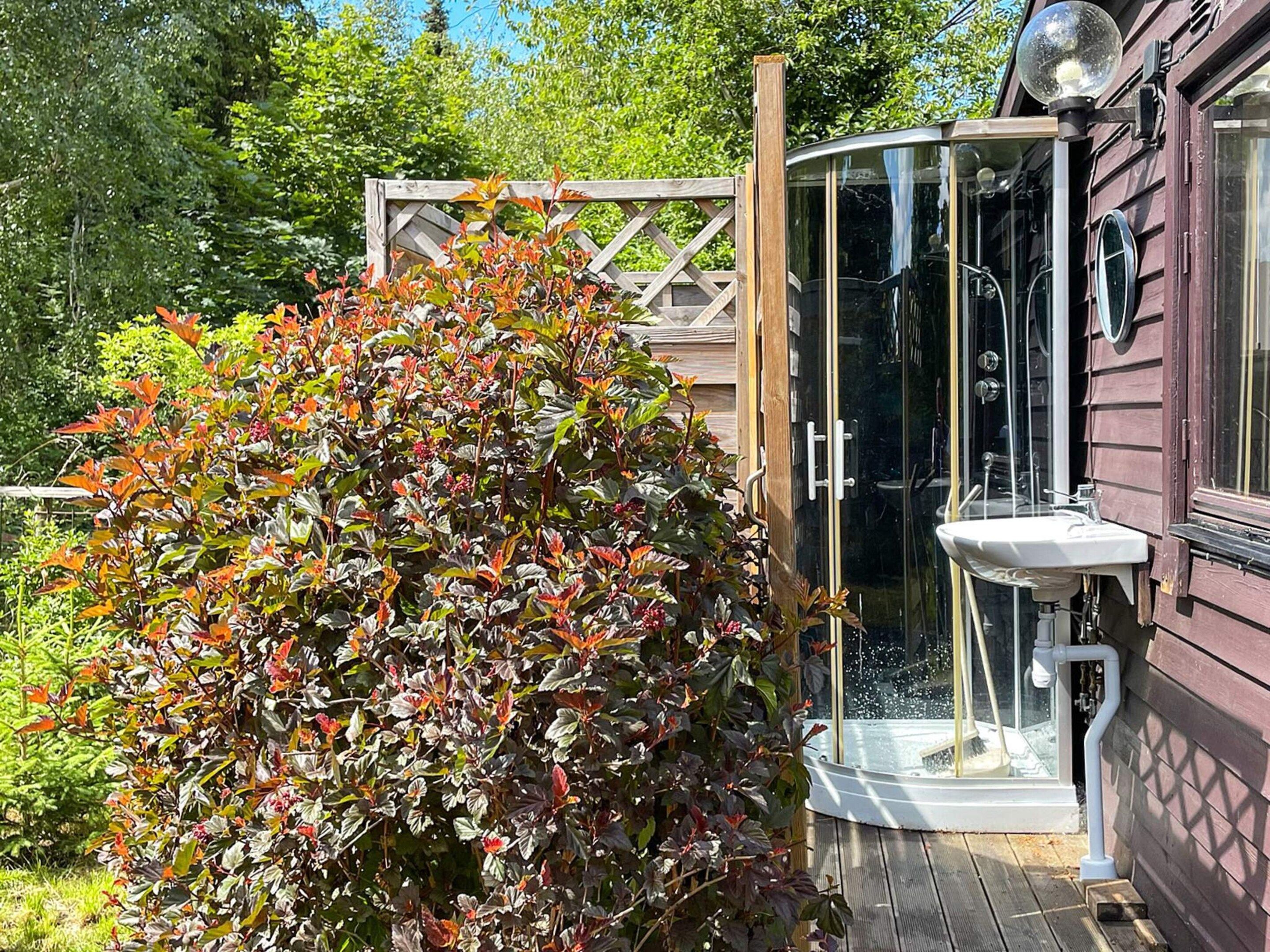A wooden deck with a glass-enclosed outdoor shower and a wooden fence.