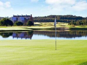 Un terrain de golf avec un mât de drapeau, un étang et un bâtiment en arrière-plan.