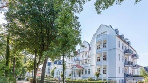 Un hotel de varios pisos con balcones, un camino empedrado y abundante vegetación.