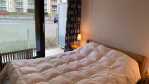 Habitación de hotel con una cama grande, ventana con vistas a un estacionamiento y edificios, cortina con un estampado y una mesita de noche con lámpara.