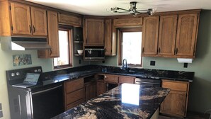 Una cocina con armarios de madera, encimera de granito negro, electrodomésticos de acero inoxidable y una ventana que proporciona luz natural.
