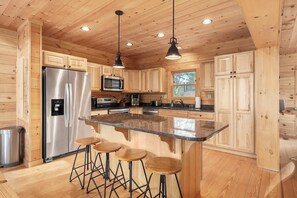 A wooden cabin kitchen with a central island, stainless steel appliances, and bar stools. - Our Mountain Retreat (Lake Lure)