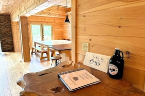 Un intérieur en bois avec une table, des chaises, un banc, une bouteille et une pancarte de bienvenue.