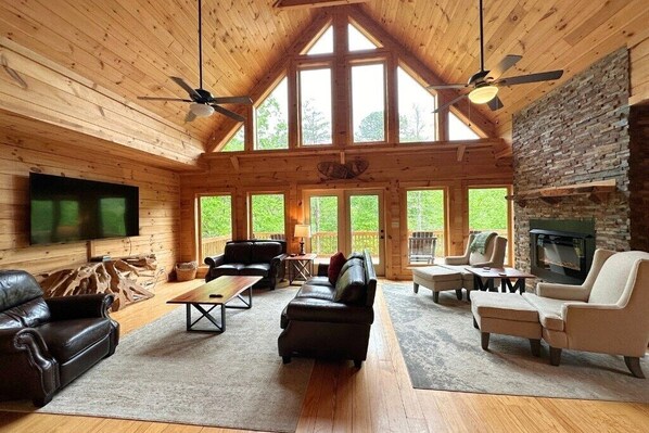 A spacious cabin with a high ceiling, large windows, a fireplace, and a TV.
