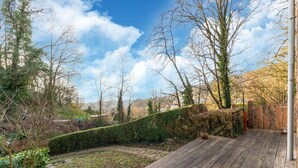 Una terraza de madera con un sendero de piedra que conduce a un área verde, rodeada de árboles y una valla de madera.