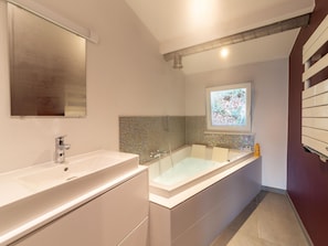 A modern bathroom with a large bathtub, a vanity with a mirror, and a decorative mosaic wall. - Magnificent Holiday Home With hot Tubs (Esneux)