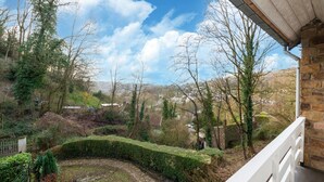 Un edificio de piedra con un balcón blanco que da a un jardín ajardinado con un sendero de piedra y diversas plantas.