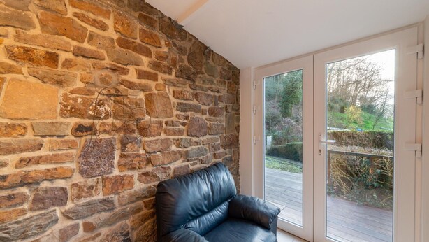 Una habitación con pared de piedra, sofá de cuero negro y puerta corrediza de vidrio que da a un espacio exterior.