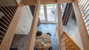 A high-ceilinged room with a wooden table and chairs, a window with blinds, and a view of outdoor seating. - Luxury new Apartment on Ameland (Buren)