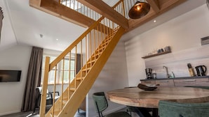 A modern interior with a wooden staircase, a round dining table, and a kitchen area. - Luxury new Apartment on Ameland (Buren)