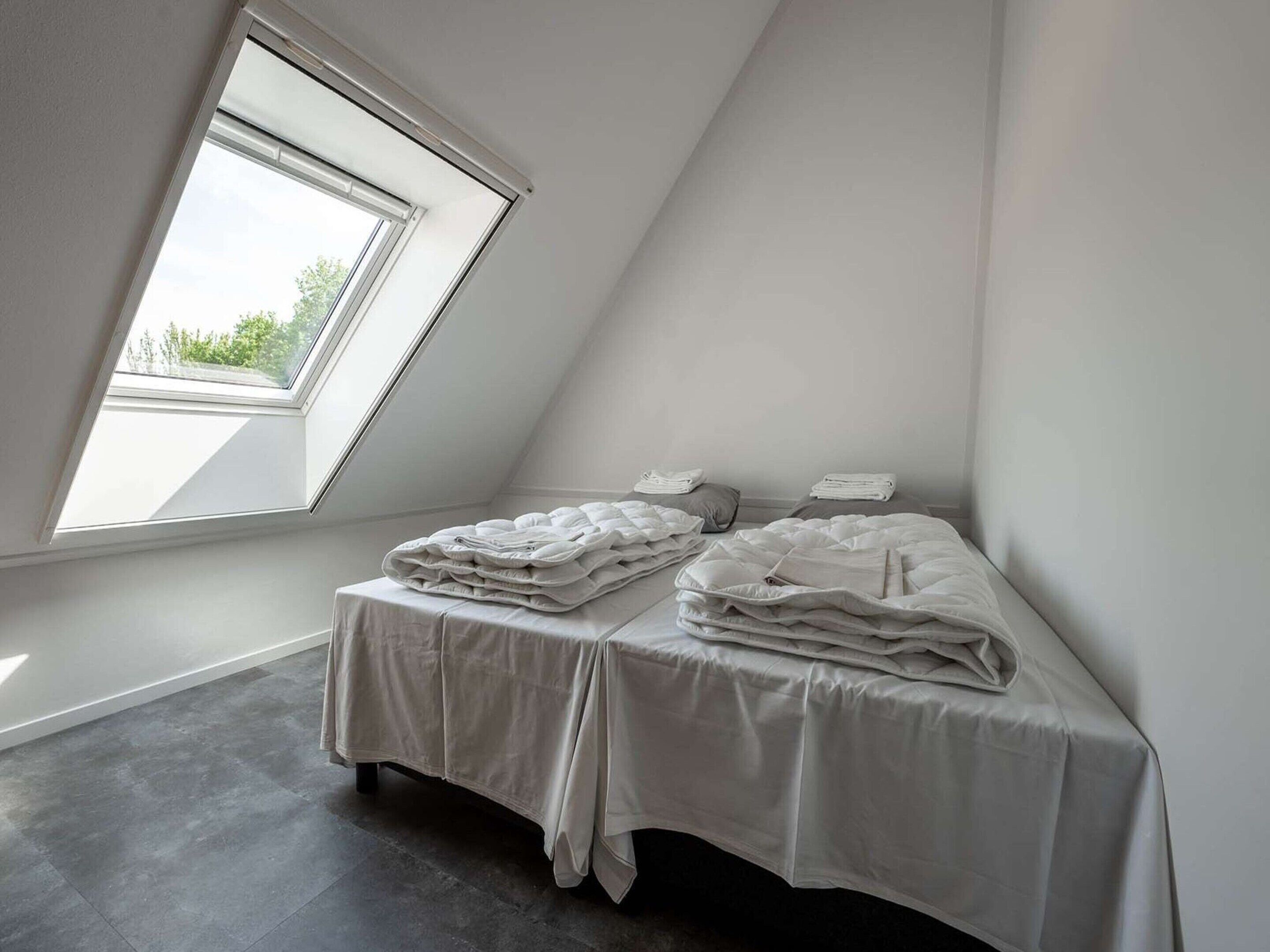 A small, modern bedroom with a skylight, two beds, and a view of greenery outside.