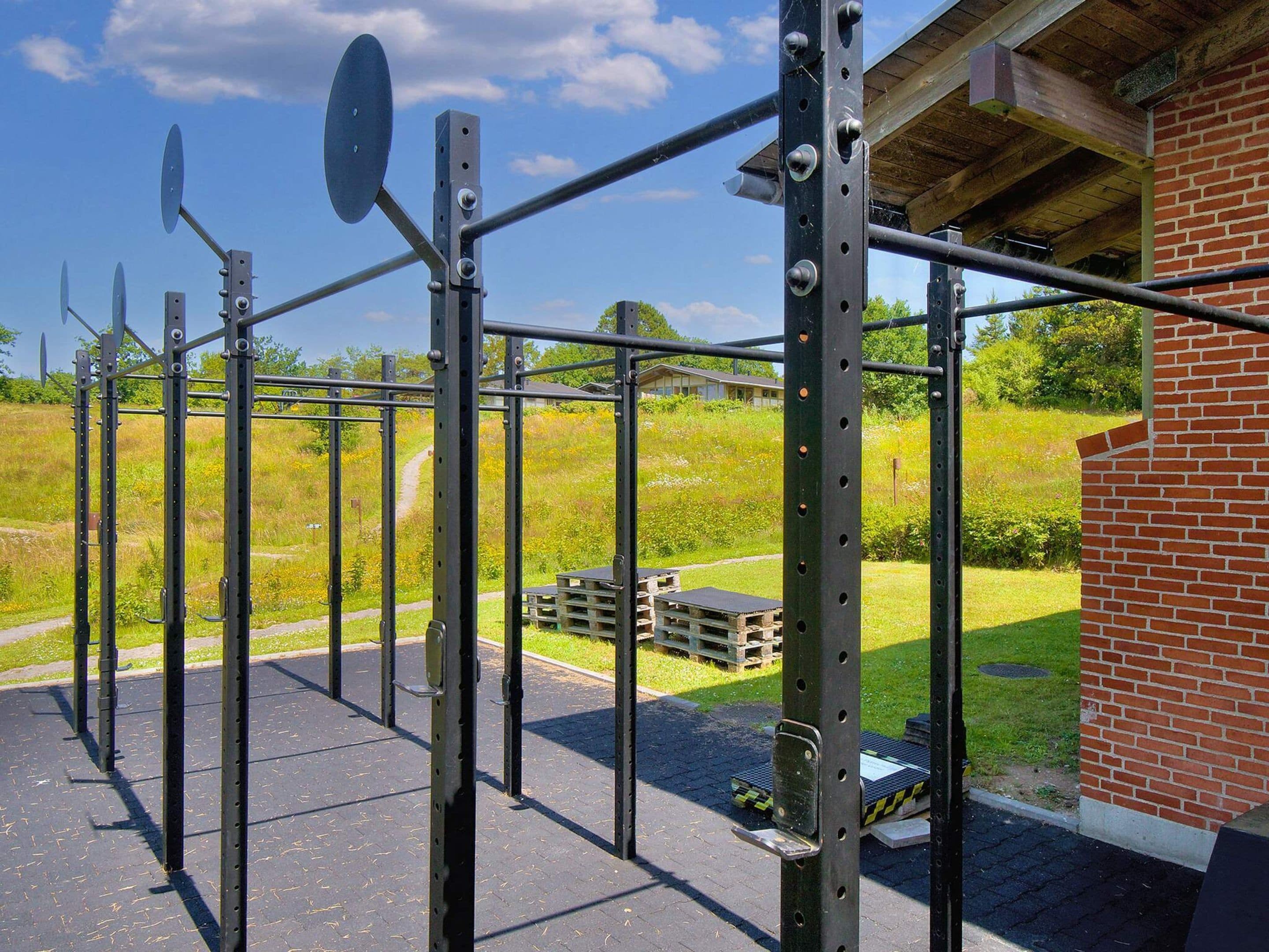 Une structure métallique abritant une salle de sport, dotée d’un toit et entourée d’un bâtiment en briques et d’un terrain herbeux.