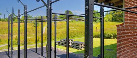 Une structure métallique abritant une salle de sport, dotée d’un toit et entourée d’un bâtiment en briques et d’un terrain herbeux.