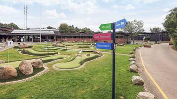 A miniature golf course with directional signs for 'Minigolf', 'Café Kyshuset', and 'Badeanstalt'.