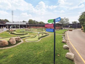 A miniature golf course with directional signs for 'Minigolf', 'Café Kyshuset', and 'Badeanstalt'. - 6 Person Holiday Park Home in Gilleleje (Gilleleje)