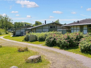 A row of single-story buildings with a gravel path leading to them, surrounded by greenery and flowering bushes. - 6 Person Holiday Park Home in Gilleleje (Gilleleje)