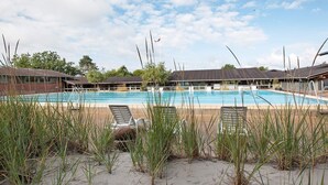 A swimming pool with lounge chairs, surrounded by tall grasses and a building with a sloped roof. - 6 Person Holiday Park Home in Gilleleje (Gilleleje)