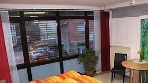 Quarto de hotel com cama, uma cadeira, uma mesinha e janela com vista para a rua.