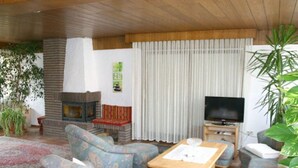 Uma sala de estar com lareira, sofá, televisão e mesa de jantar.