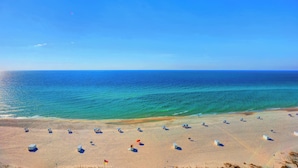 Una platja amb nombroses gandules i ombrel·les, un cel serè i l'oceà al fons.