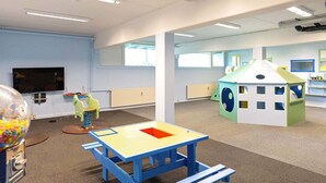 A brightly lit playroom with a blue table, a green playhouse, and a television on the wall. - 6 Person Holiday Park Home in Ringkobing (Ringkobing)
