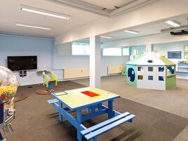 Una sala de juegos bien iluminada con una mesa azul, una casita de juegos verde y un televisor en la pared.