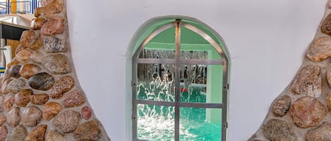 A stone wall with a window featuring a green frame and a view of a building with a green facade.