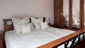 A bedroom with a large bed, multiple pillows, a wooden wardrobe, and a nightstand. - Cozy Apartment With Fireplace and Balcony (Brilon)