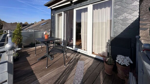 A modern house with a balcony featuring a table and chairs, a potted plant, and a view of the surrounding area. - Cozy Apartment With Fireplace and Balcony (Brilon)