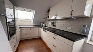 A modern kitchen with white cabinets, a black countertop, and wooden flooring. - Cozy Apartment With Fireplace and Balcony (Brilon)