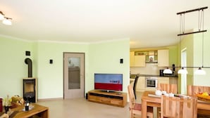 A living room with a TV, wooden furniture, a fireplace, and a kitchen in the background. - Apartment in Tisens (Putbus)
