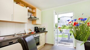 A modern kitchen with white cabinets, a microwave, a coffee maker, and a dining area with a table and chairs. - Apartment in Tisens (Putbus)