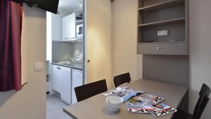 A compact kitchenette with a microwave, sink, and dishwasher. There is a dining table with chairs and a bowl. Shelves above the table hold a few items. - Ski-in/ski-out & foot of the slopes, 3rd floor, tv, 28m², La Plagne (La Plagne)
