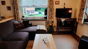 Ett vardagsrum med en soffa, ett soffbord, en tv och ett fönster med utsikt över ett hus och en bil utanför.