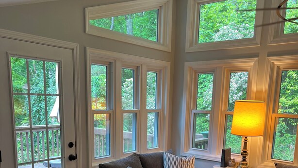 A cozy living room with a gray sofa, patterned pillows, a wooden coffee table, and a rug. Large windows offer a view of greenery outside. - Serenity Home - Forest, Fun, and Adventure (Brevard)