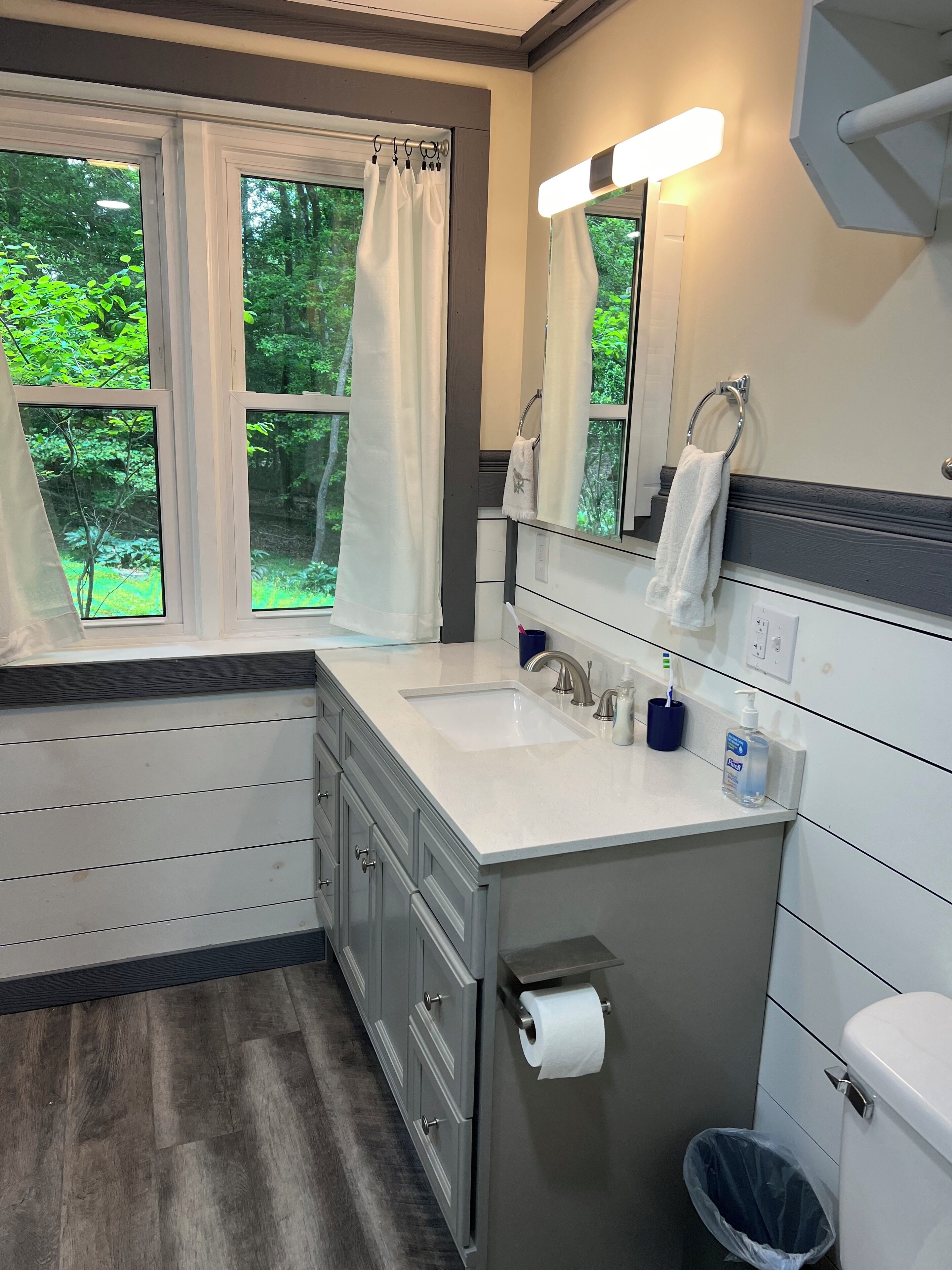 A bathroom with a window, a sink, a toilet, and a trash can.