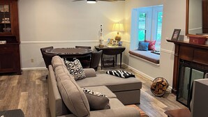 A living room with a sectional sofa, a dining table with chairs, a fireplace, and a ceiling fan. - Serenity Home - Forest, Fun, and Adventure (Brevard)