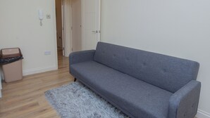 Ett rum med en grå soffa, en mjuk matta, en papperskorg och en dörr som leder till ett annat rum.